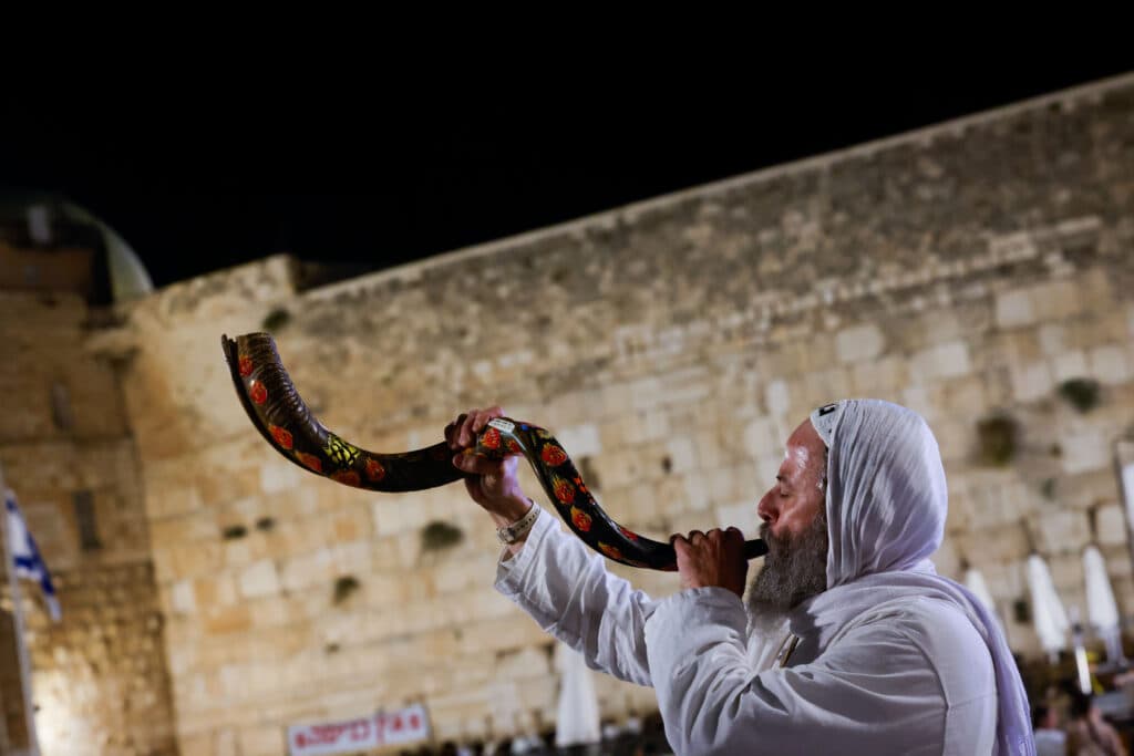man blowing shofar at western wall during slichot
