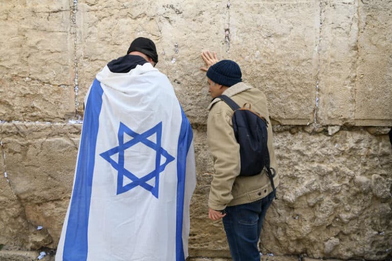 Two men praying at the Western Wall. One man is draped in an Israeli flag.