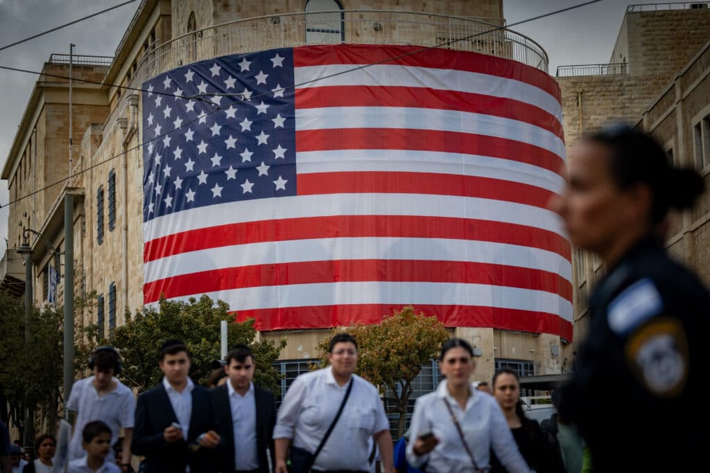 People walk near a large American flag in Jerusalem.