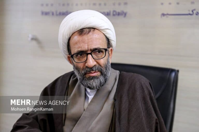 Iranian politician Ali Salimi sits indoors wearing clerical clothing and glasses.
