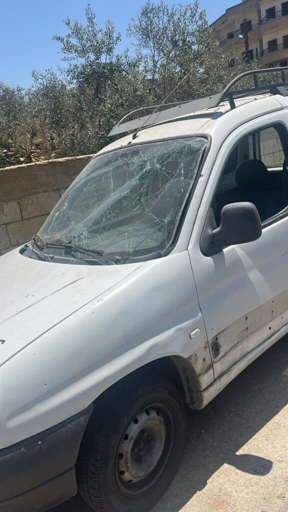 A white vehicle with a shattered windshield and visible damage on the side.