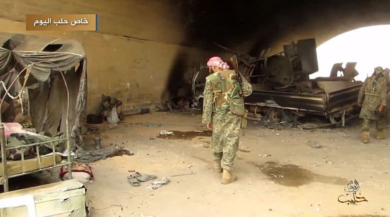 Armed fighters walking through the Abu al-Duhur airbase in Syria after battle damage.