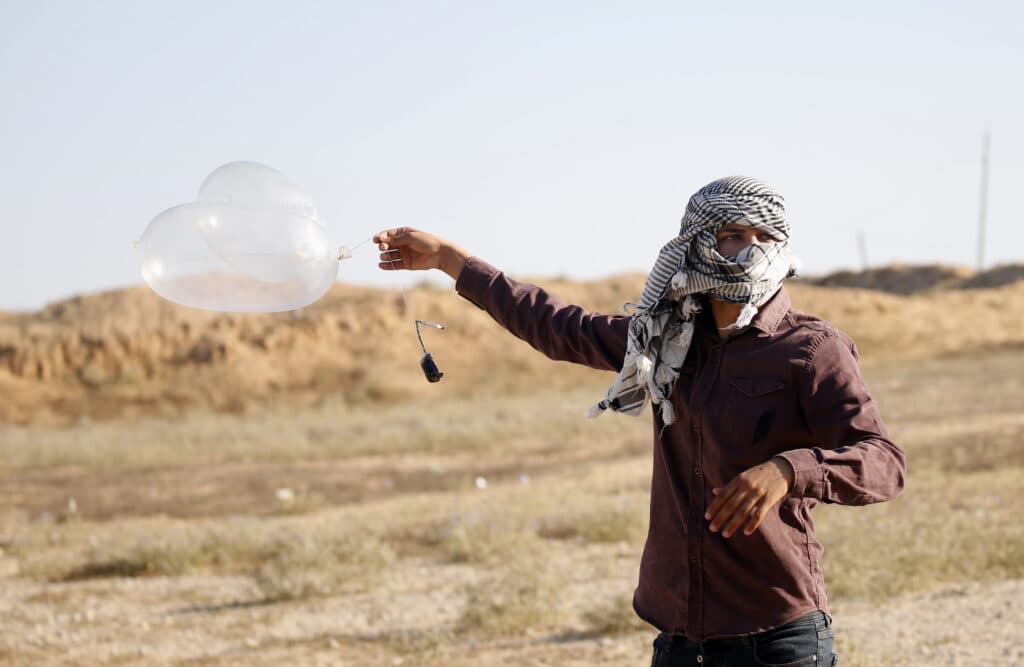 A masked Palestinian man holding balloons near Rafah along the Israel-Gaza border.