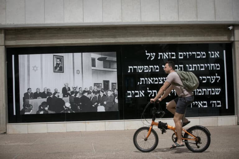 man on bike rides past poster of declaration of state of israel in tel aviv