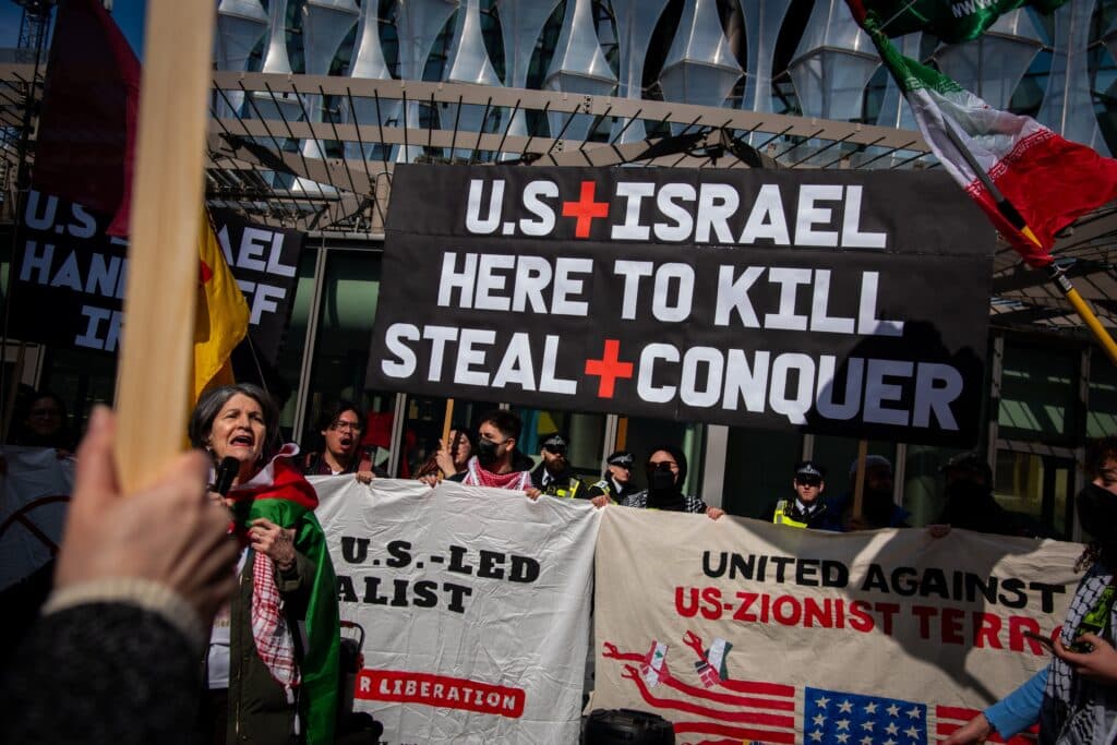 Anti-Israel protesters holding banners and signs at a demonstration.