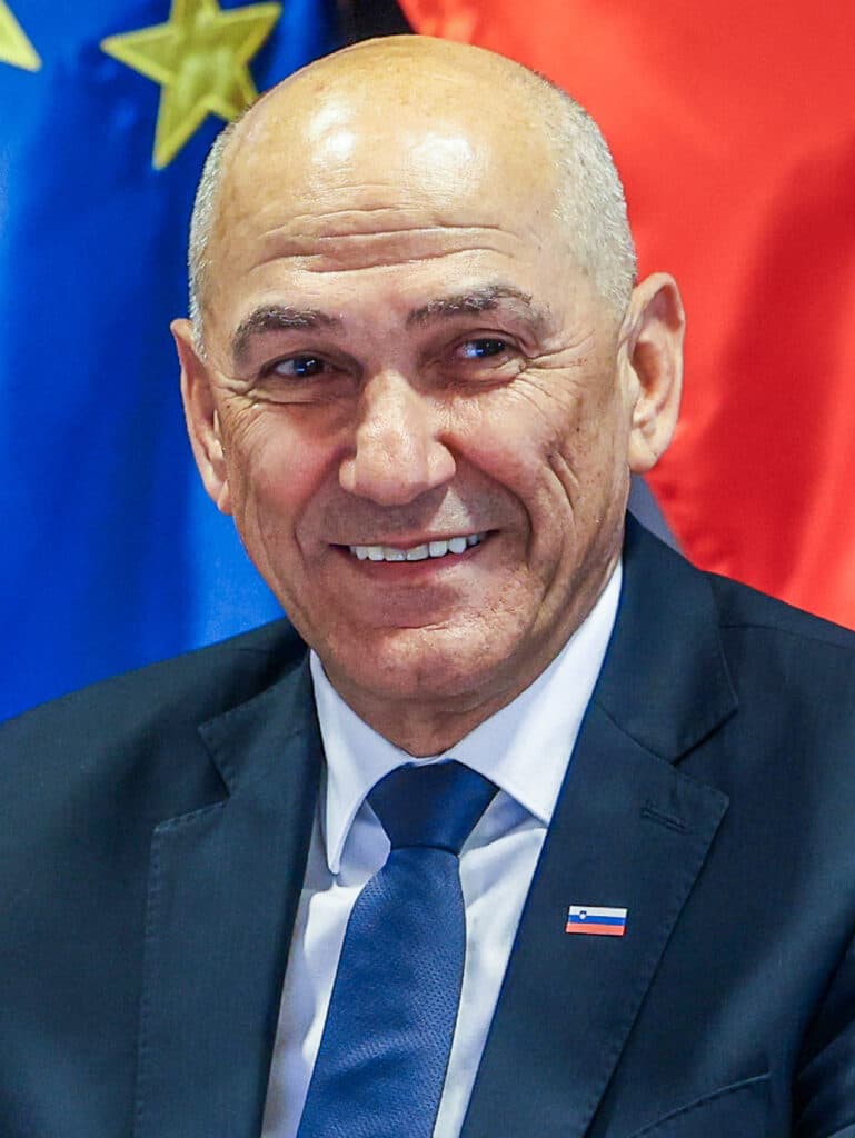 Slovenian Prime Minister Janez Janša smiling in front of Slovenian and European Union flags.
