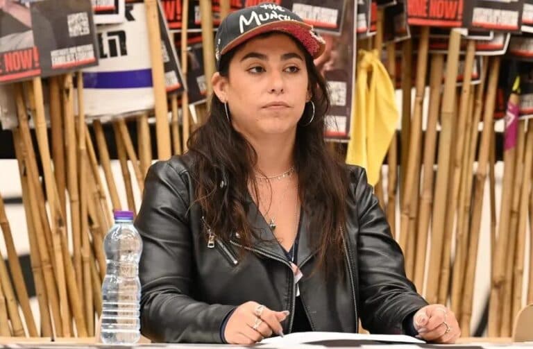 Ilana Gritzewsky seated before posters of hostages.