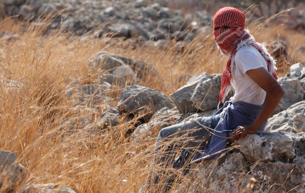 A young Palestinian with a covered face sits on rocks near Ni'lin.