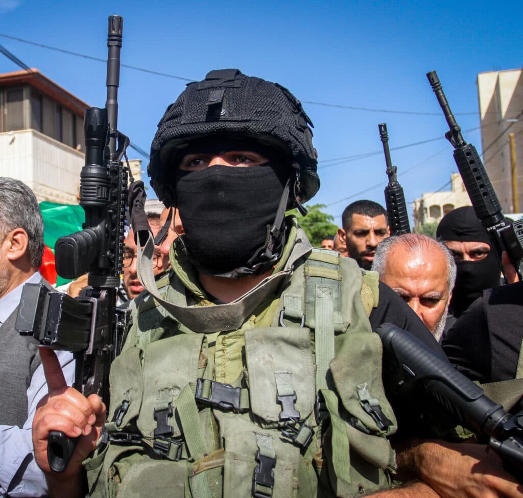 Armed masked Palestinian militant standing among civilians in Jenin