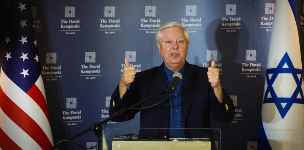 U.S. Senator Lindsey Graham speaks at a press conference in Tel Aviv with American and Israeli flags behind him.