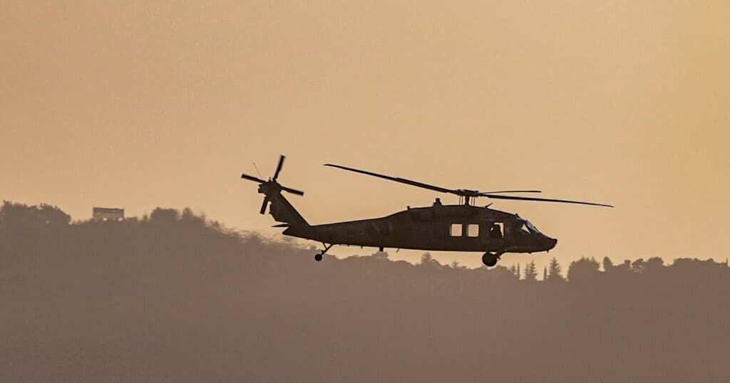A military helicopter flying near the Israel-Lebanon border at sunset.