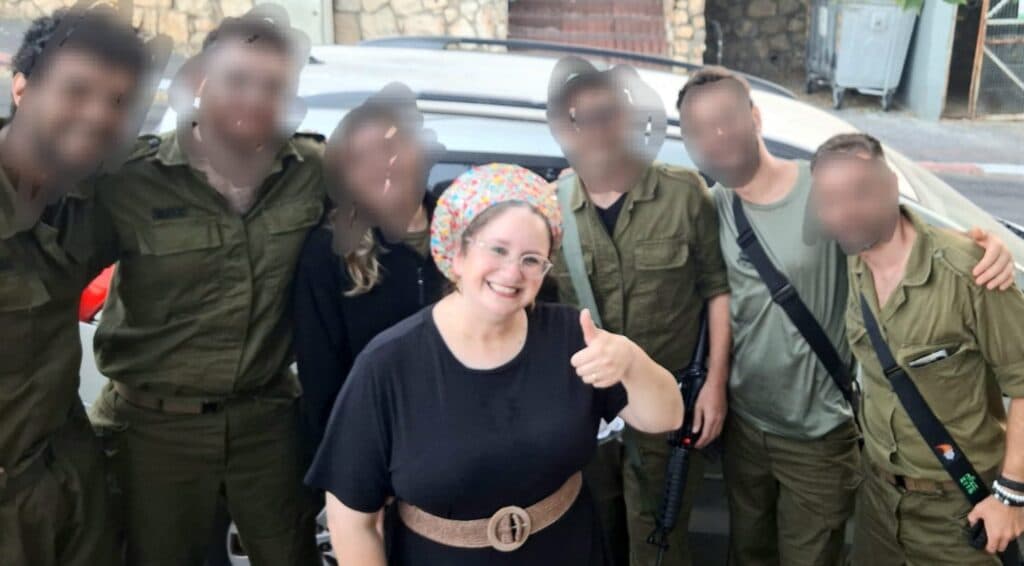 Neta Ben Amram smiles with soldiers in a photo, with several faces blurred.