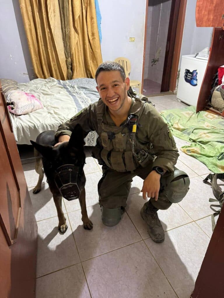 Capt. David Hazut smiling while wearing an IDF uniform with his dog, a large German Shepherd.