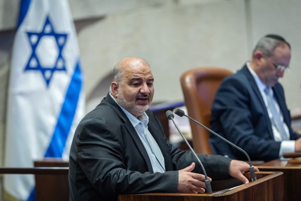 MK Mansour Abbas speaks at the Knesset plenum beside an Israeli flag.
