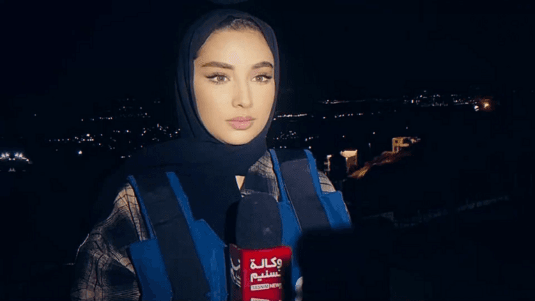 A Tasnim News correspondent holds a microphone while reporting at night.