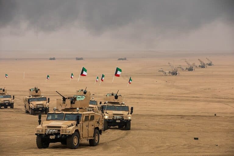 Kuwaiti military vehicles with national flags move through the desert during a counter-drone exercise.