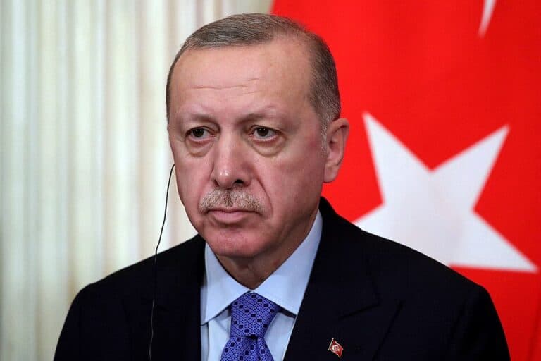 Turkish President Recep Tayyip Erdoğan sits in front of a Turkish flag.