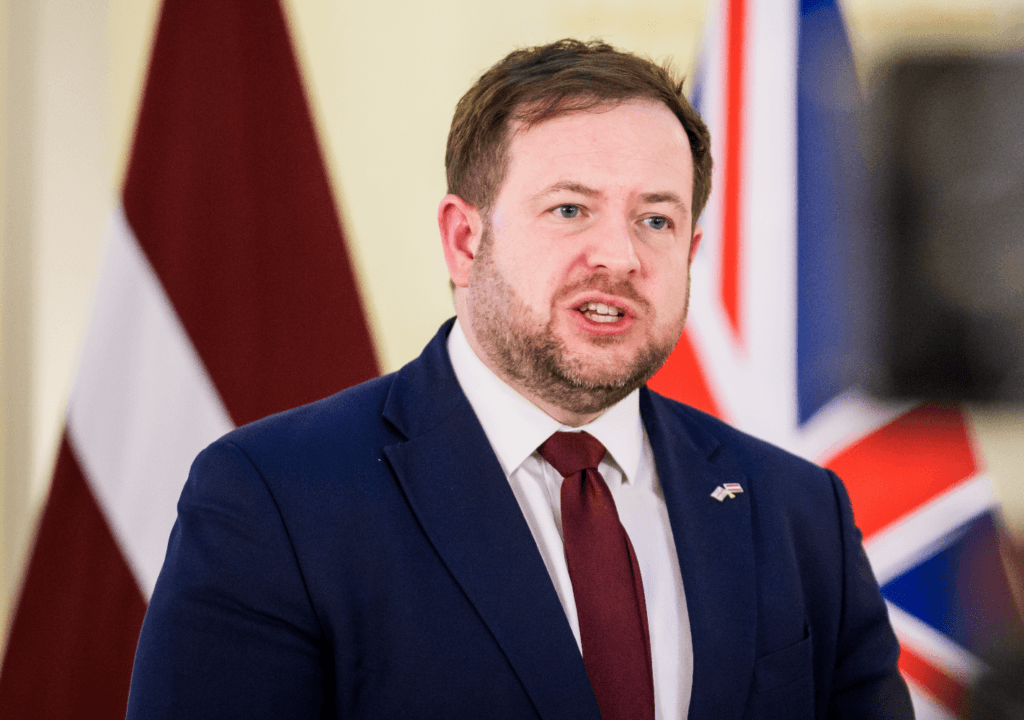 Stephen Doughty speaks with British and diplomatic flags behind him.