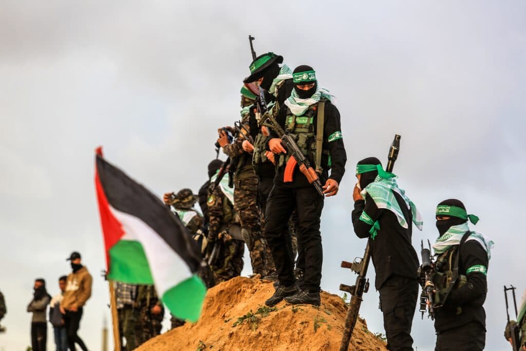 Armed Hamas terrorists stand on a mound near a Palestinian flag.