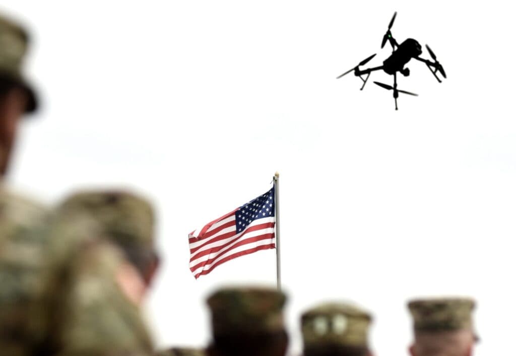 A U.S. drone flies above American military personnel and a U.S. flag.