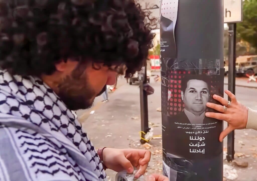 Hezbollah supporters in Beirut standing near a poster of Lebanese MP Nadim Gemayel.