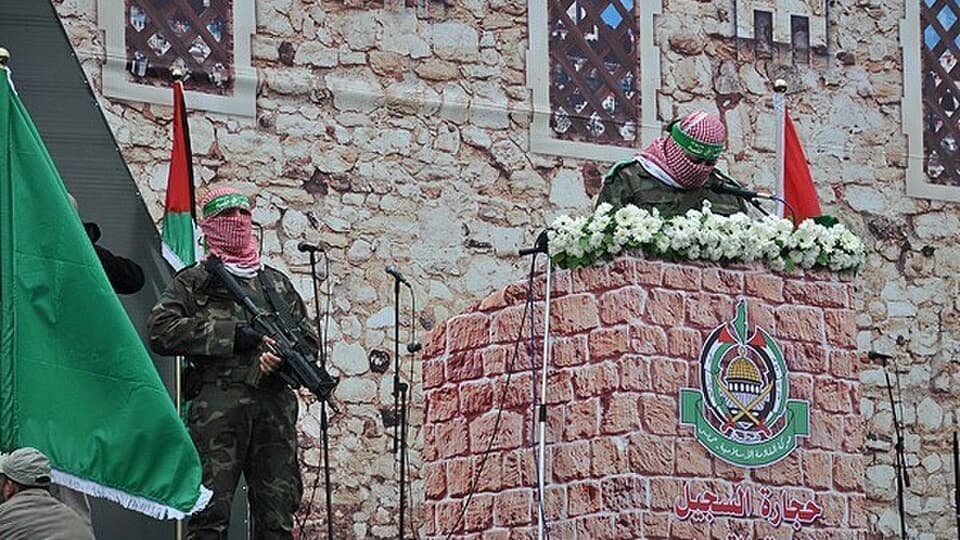 Masked Hamas members stand beside Palestinian and Hamas flags during a rally in Gaza.
