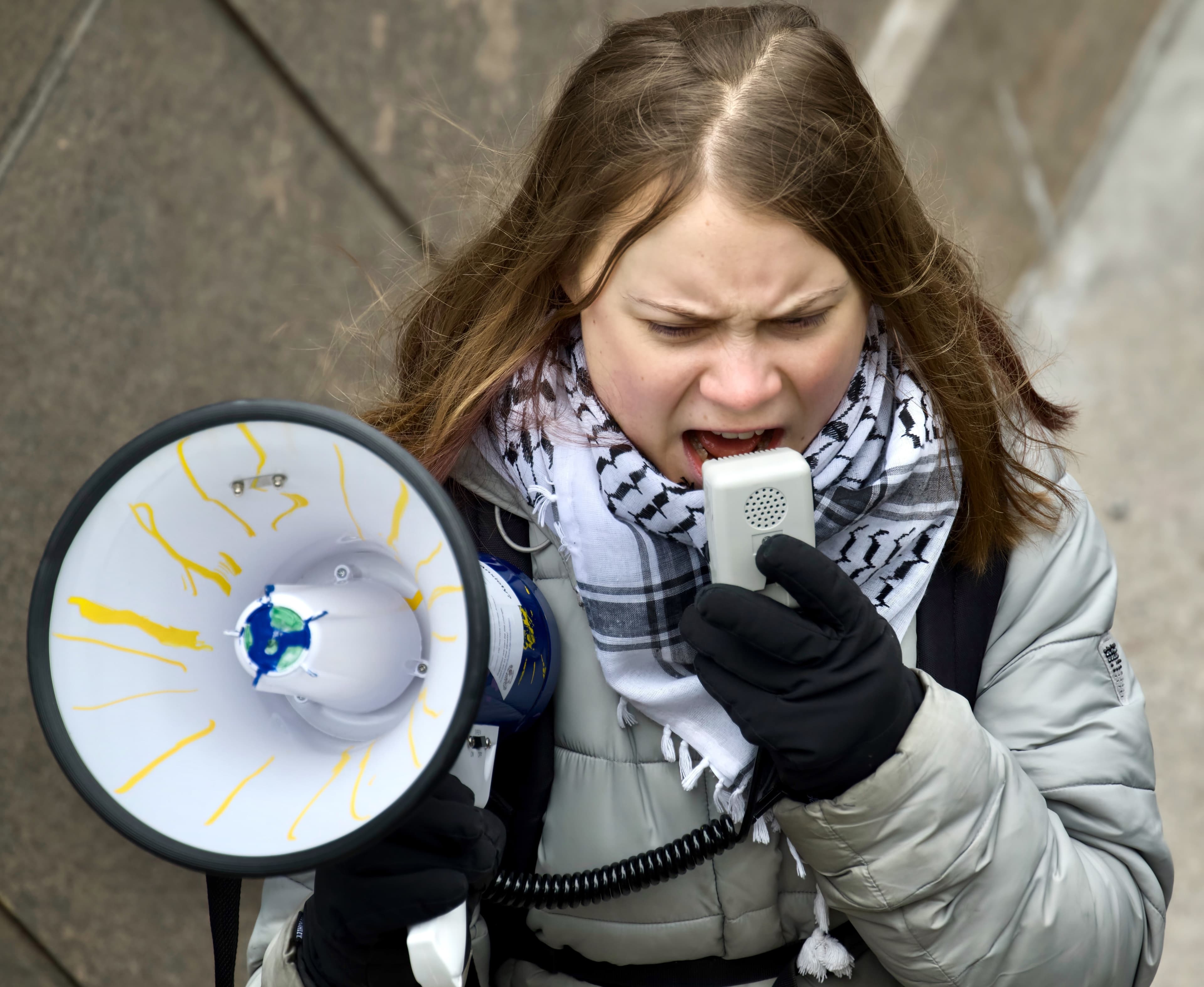 Greta Thunberg speaks through a megaphone while wearing a black-and-white keffiyeh.